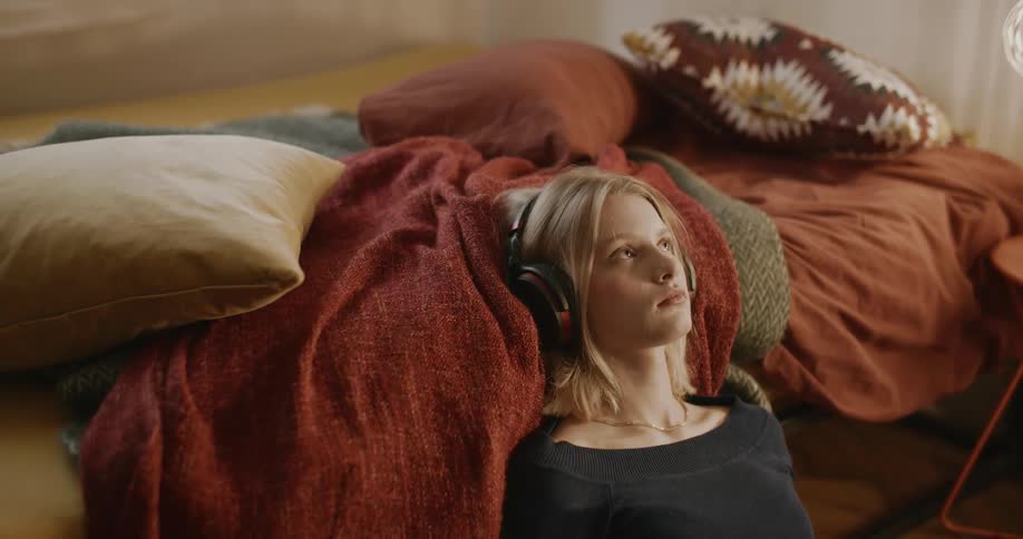 Teenage girl wearing headphones checks her phone in the bedroom