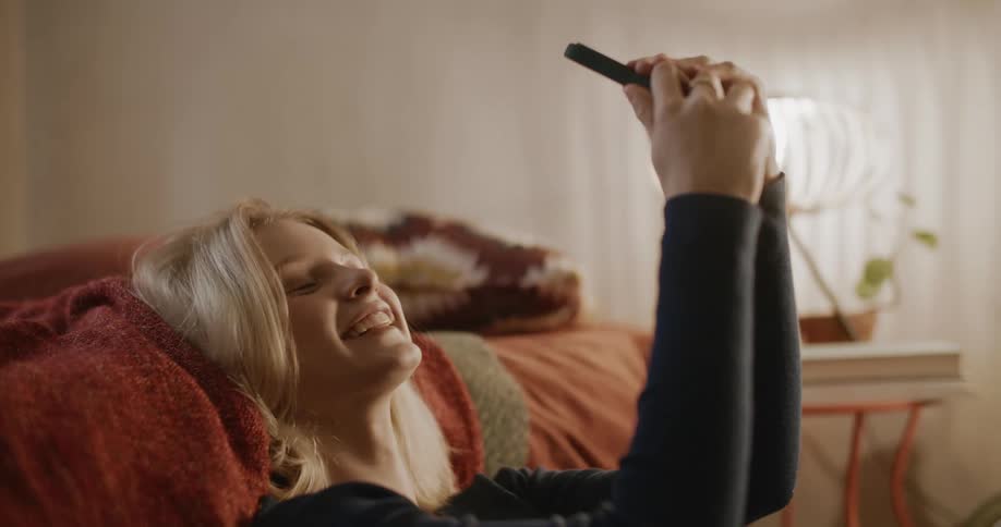 Teen smiles while seated on the bedroom floor taking selfies at midday