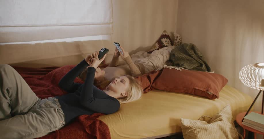 A teenager and a child lying in bed playing on their cell phones