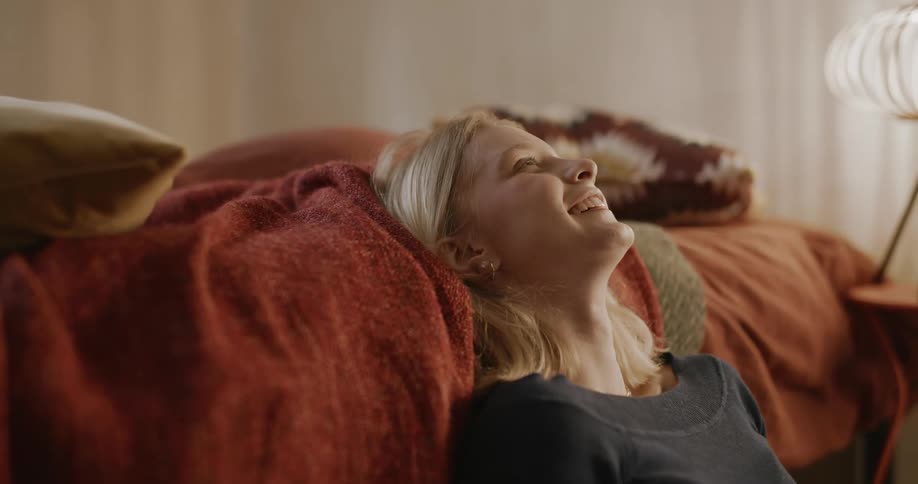 A blonde teenage girl laughs and puts her head back on a bed