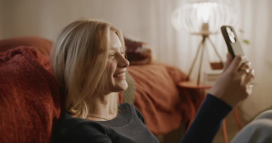 A teenage blonde girl smiling while using her cell phone