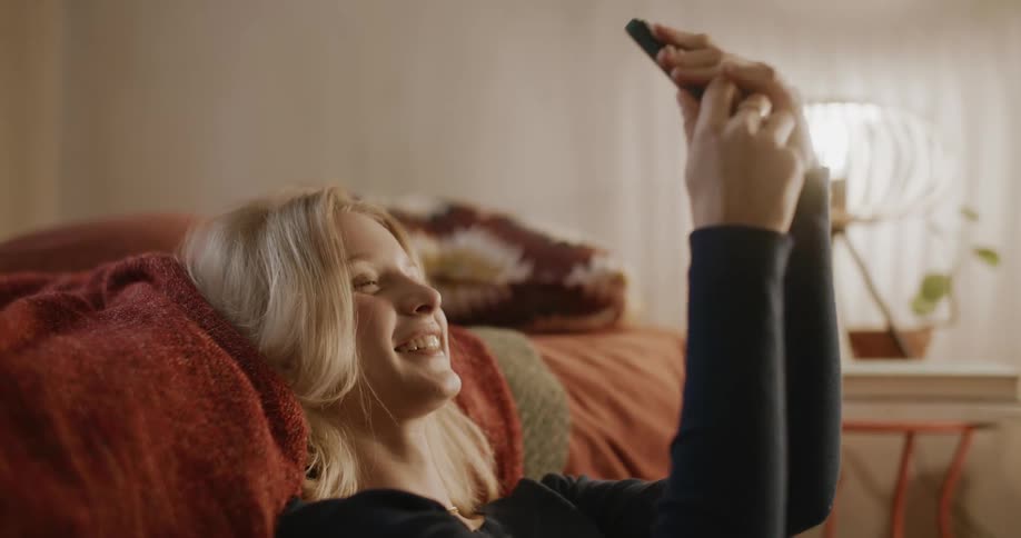 A blonde teenager smiles and takes a selfie with a phone