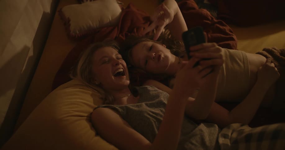 Portrait of a young woman and a girl smiling and taking a selfie while lying in bed
