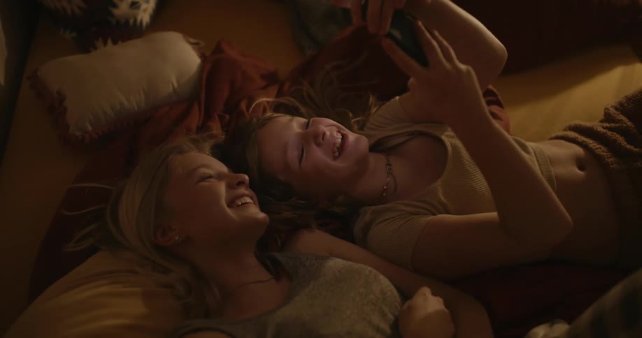 Friends are lying in bed watching videos on their cell phones