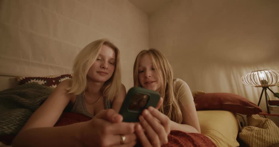 Girls lying in bed playing on their cell phones