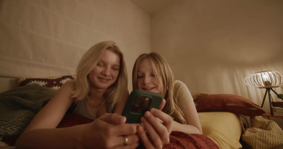 Woman and a young teenager lying in bed and both smiling giving their cell phones