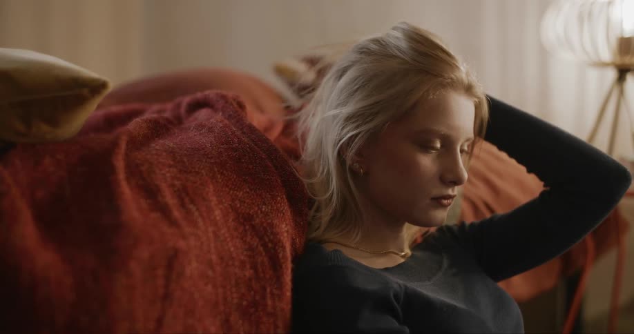 Portrait of a young blonde woman sitting on the floor next to the bed messing with her hair