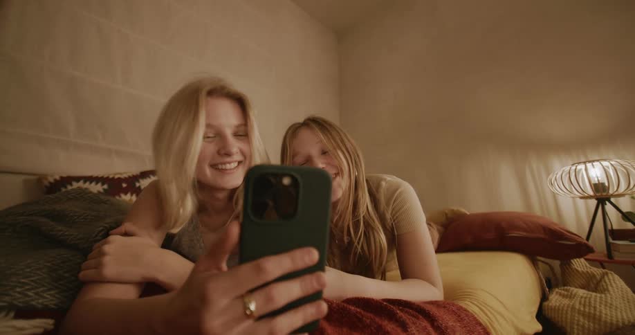 Portrait of a woman and a child both lying in bed and smiling a lot watching on their cell phone