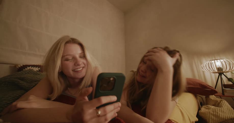 Portrait of a young woman and a girl lying in bed smiling and using a cellphone