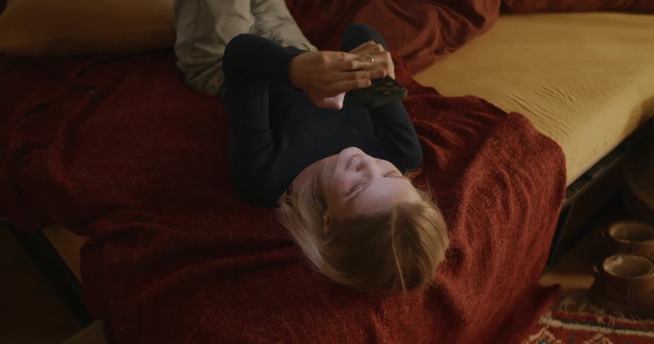 A teen girl relaxing on a couch with a red blanket and a smartphone