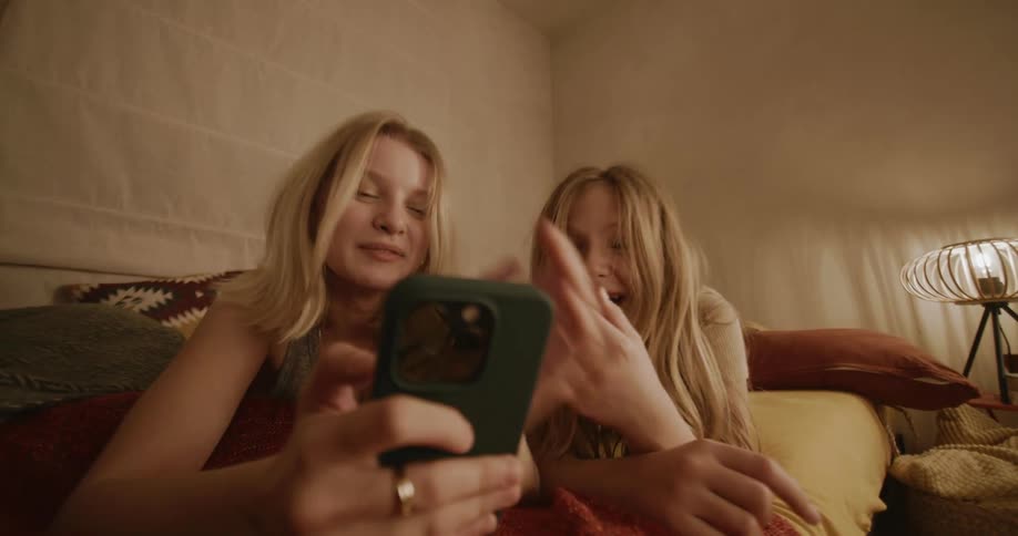 Two teenage girls laugh while using a smartphone