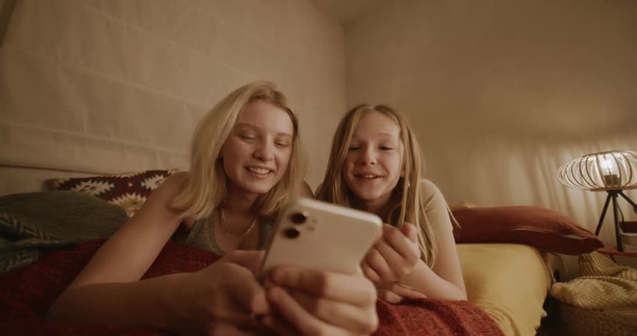 Portrait of a young woman and a child both blonde lying in bed using their cell phone smiling