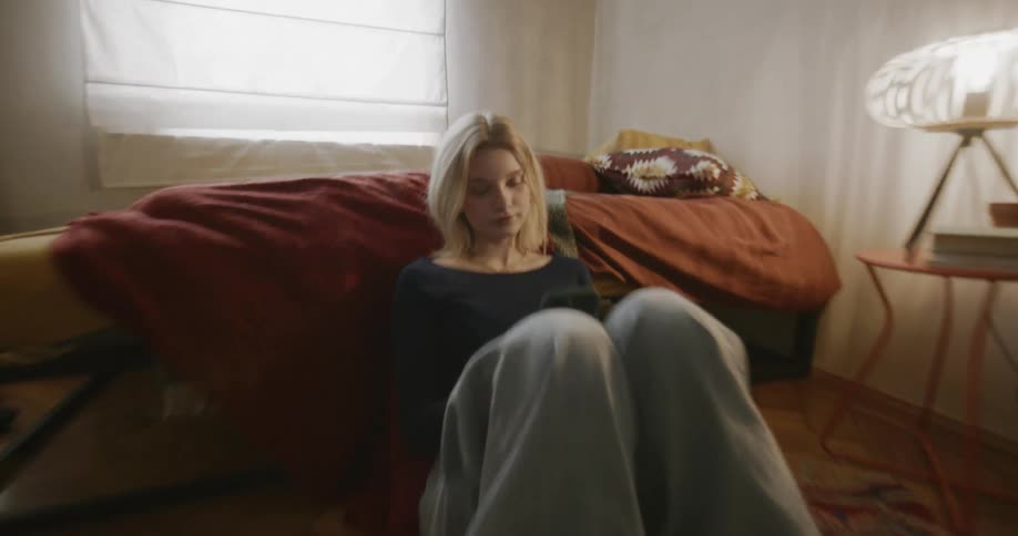 Young woman holding a phone reclined the bed wearing a knitted sweater