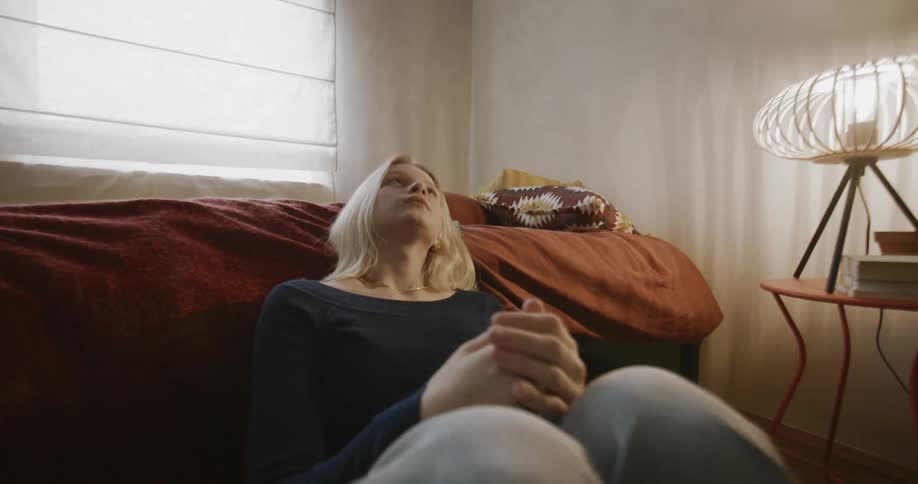 Portraits of a young blonde woman sitting on the floor next to her bed in the bedroom