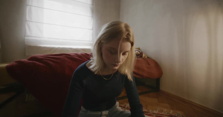 Portrait of a young blonde woman sitting on the floor of a bedroom using her cell phone