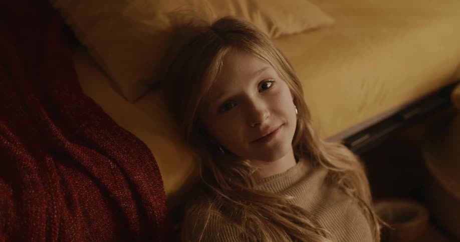 Portrait of a young blonde teenage girl sitting next to the bed giving a slight smile