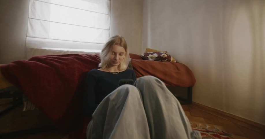 A young woman checking her phone in the bedroom floor