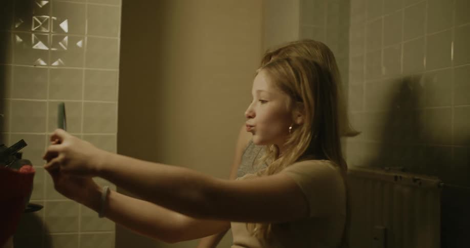 Two young girls inside the bathroom taking out their cell phones and taking a selfie