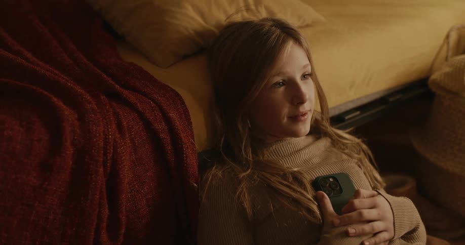 Portrait of a young girl sitting on the floor next to the bed using her cell phone and then taking a deep breath
