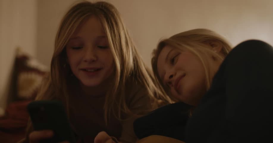 Teenagers look at a cell phone together in bed