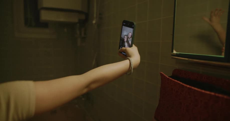 Two blonde girls hugging each other who are taking photos on a cell phone inside a bathroom