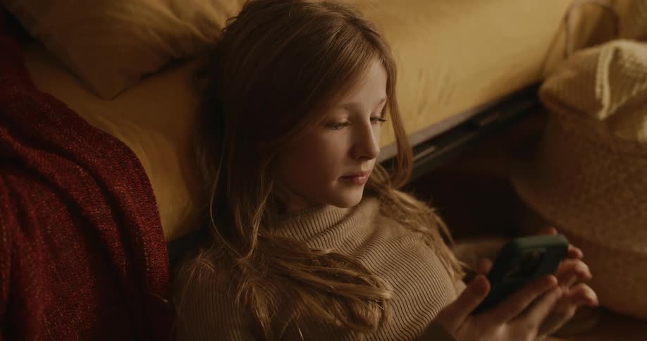 Teenage girl reclined on a bed checks her phone