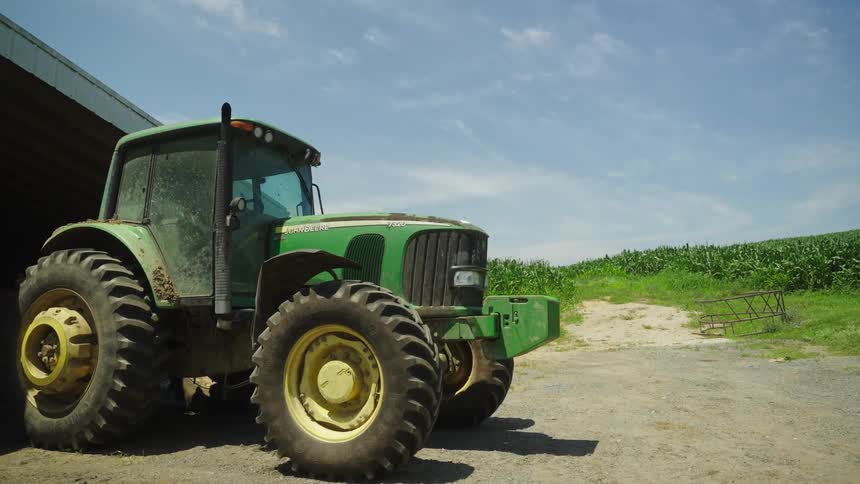 A green tractor is positioned near a lush green field