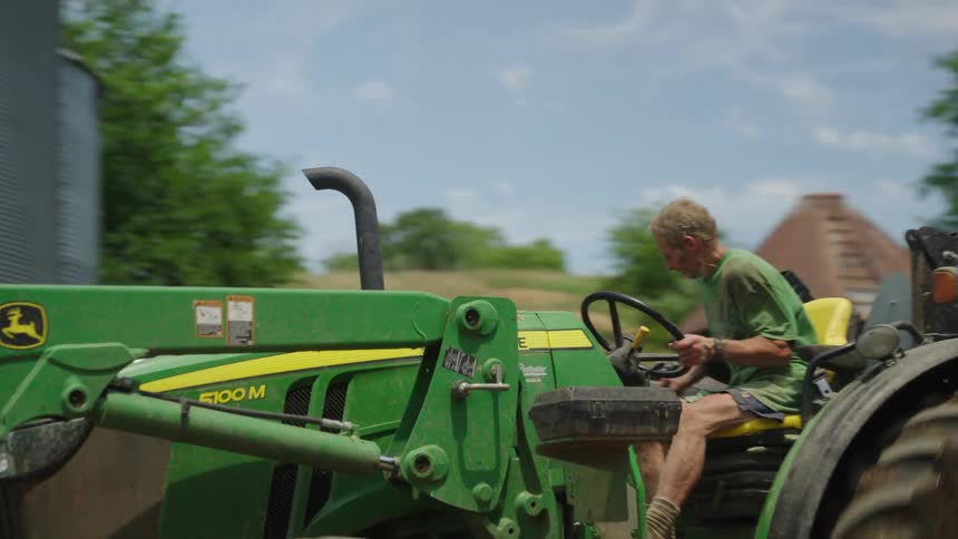 A person driving a green bulldozer on a farm near a granary