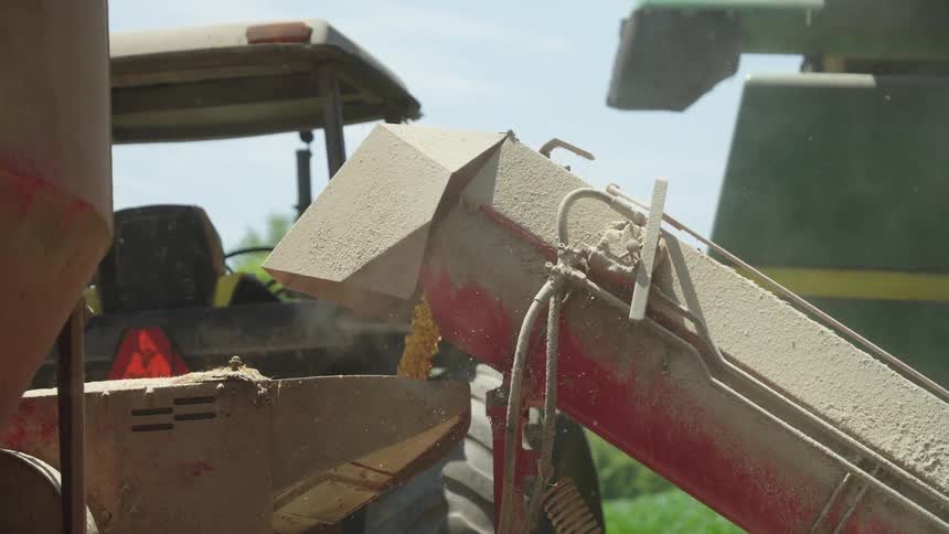 Farm machinery fills bin releasing dust into the air