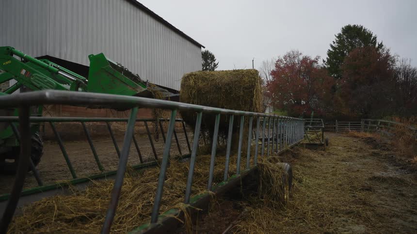 A person harvesting hay with a tractor on a farm on a cloudy day