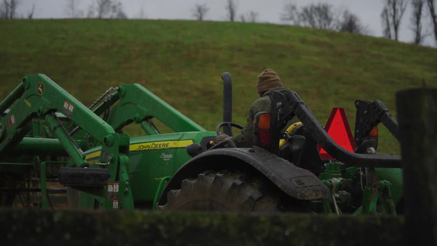 Man steps down from a farm tractor after parking it at midday