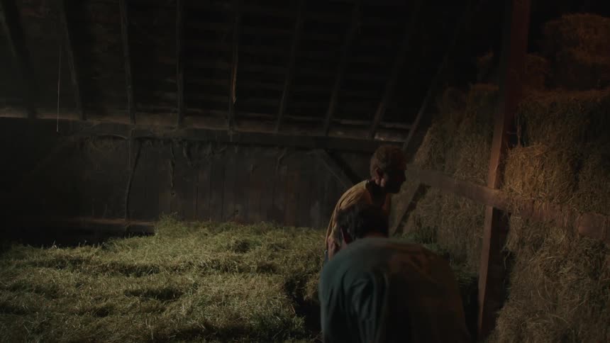 Two men move hay in the barn