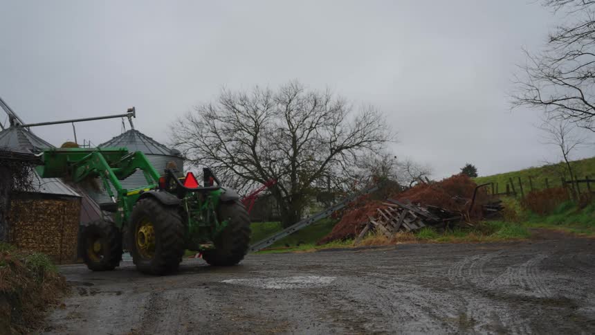 A man drives a tractor with a lift on it into around a farm