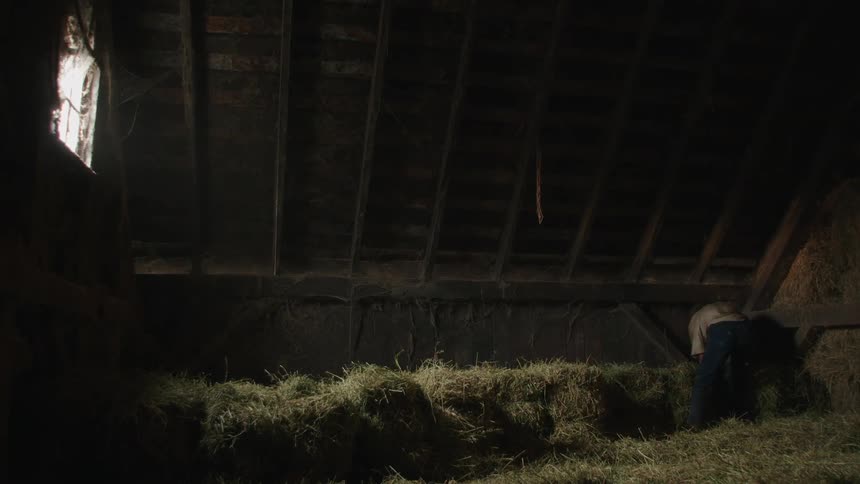 A farmer handling hay bales in the barn