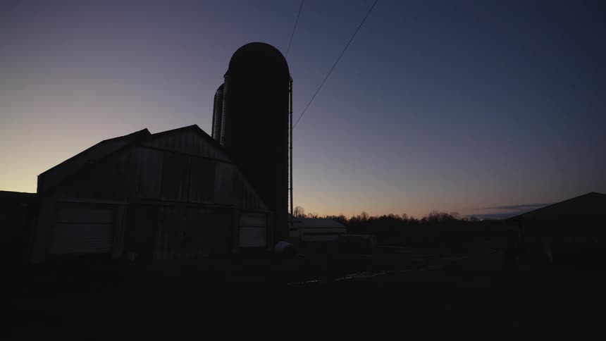 Silhouette of a silo next to a barn in a farm at sunset