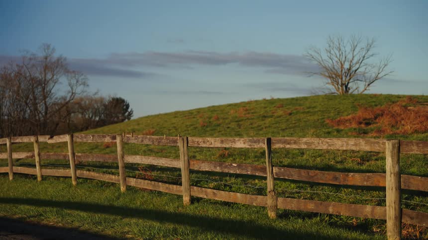 Wooden country fence along a rural hillside with trees in the distance
