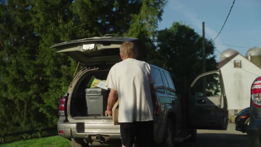 A man walking between two parked cars with their trunks filled with bags and boxes