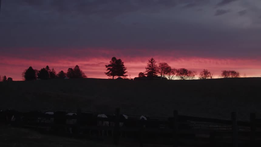Farm with cows on an open ranch overlooking a reddish dawn sky