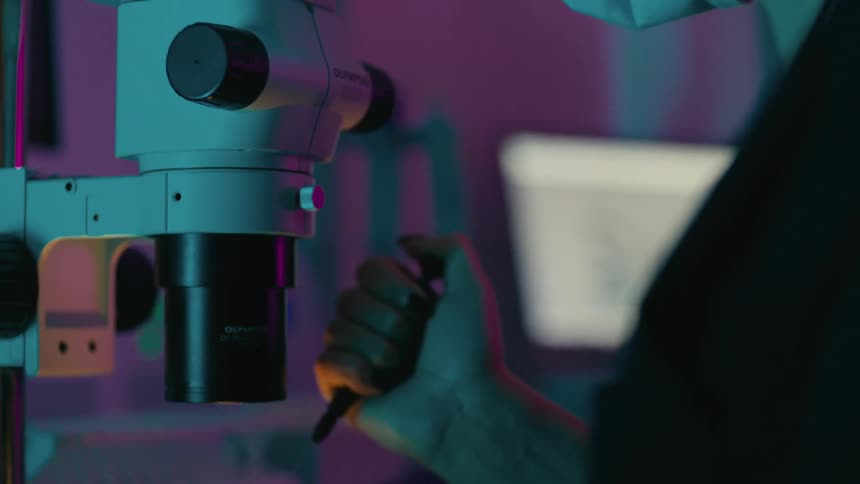 Concentrated woman applying needle end to a capsule and observing through microscope