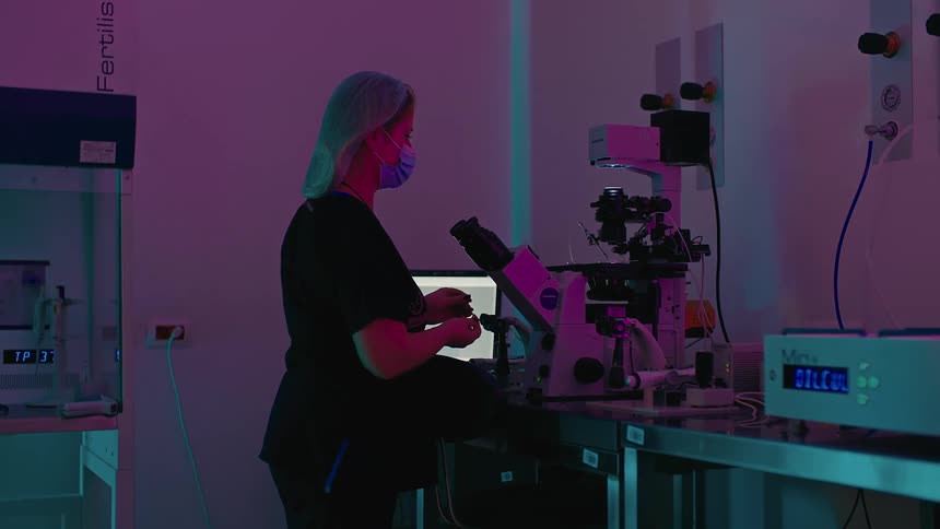 A woman sits in front of the microscope