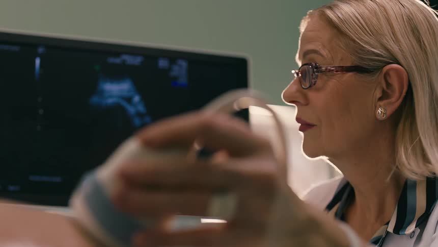 A doctor is conducting an ultrasound scan with the monitor displaying the image in the background