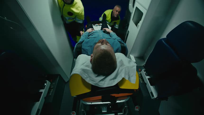 Two paramedics are attending to a patient on a stretcher inside an ambulance at night