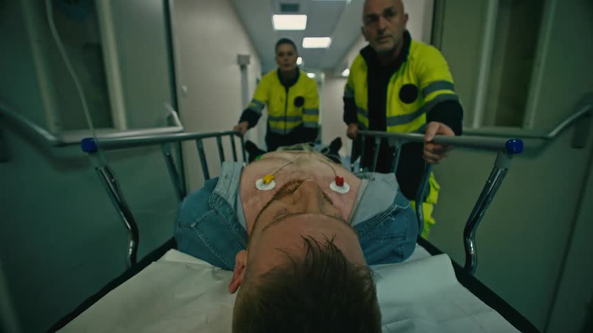 Two outpatient workers carrying a sleeping man on a stretcher down a hospital corridor