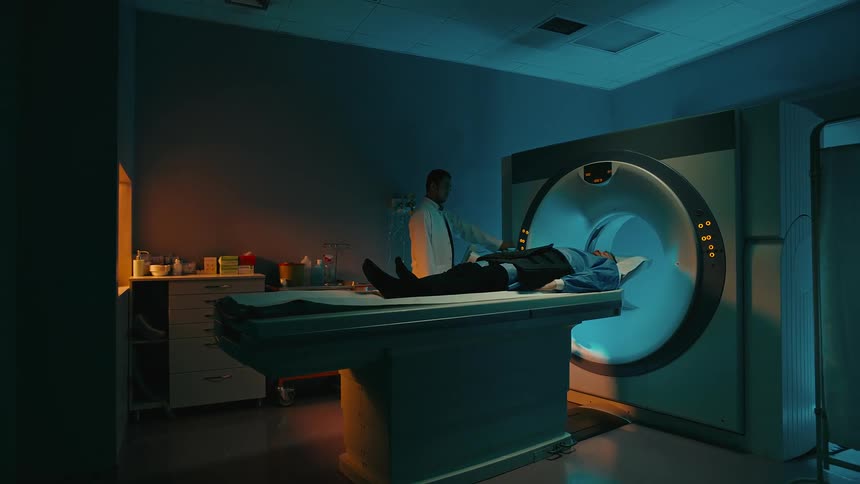 Medical professional monitors mri machine while patient lying on bed enters it