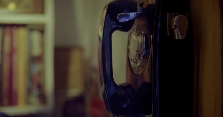 Wall mounted vintage  telephone with an out of focus bookshelf in the background