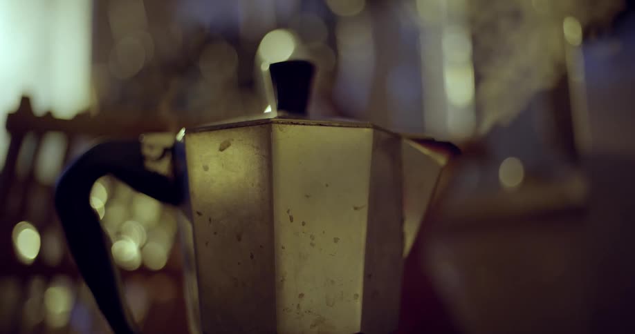 A closeup of a used percolator steaming with a bokeh background