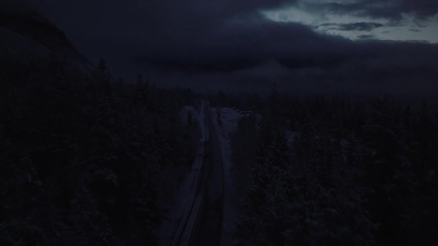 Aerial panorama of a street in the middle of a forest covered by snow and a dark cloudy sky
