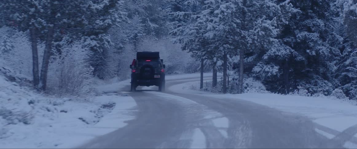 Pickup trucks traveling on a narrow street in the middle of a forest covered in snow