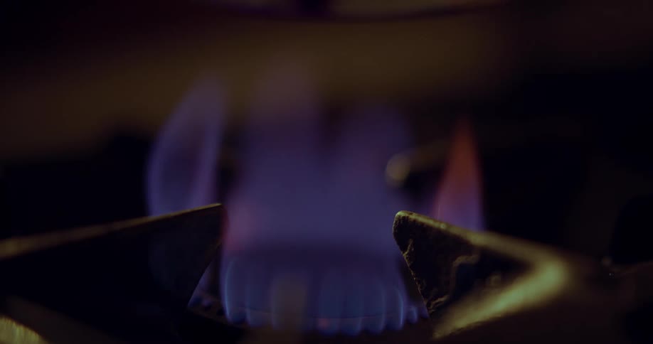 Slow motion close up of a gas flame as a coffee pot is set down on top of it