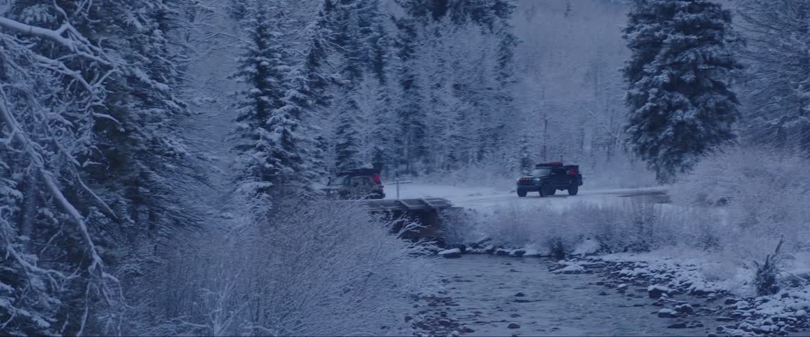 Two sports trucks passing on a street in the middle of a forest covered in snow